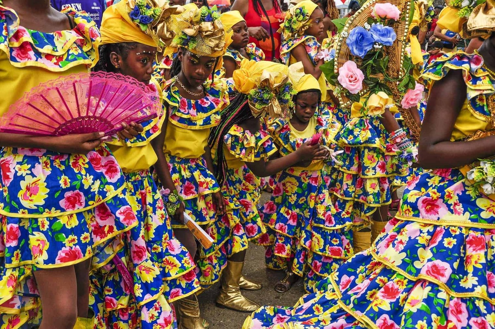 A group of young ladies are dressed in yellow, blue and pink frilly Spanish-styled dresses with head-ties and flowers some carrying fans on Carnival in Trinidad representing the country's Spanish cultural heritage.