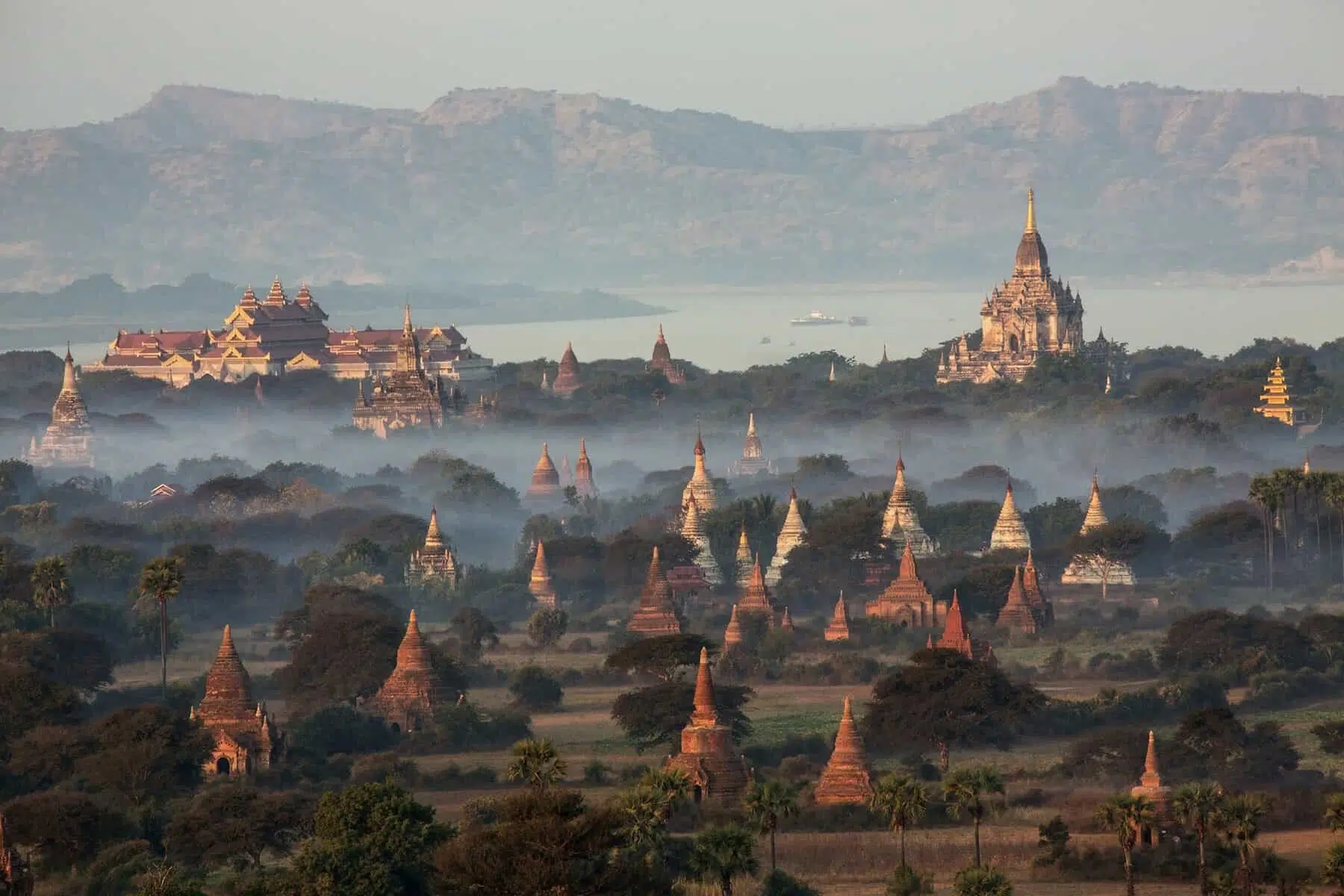 Hot air balloons flying over the temples of the Archaeological Zone in Bagan in the early morning sunlight. In the distance is the Irrawaddy River. Myanmar (Burma).