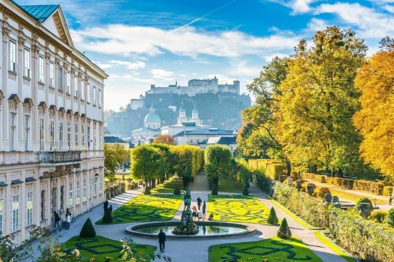 Historic European castle with lush garden and vibrant autumn foliage.