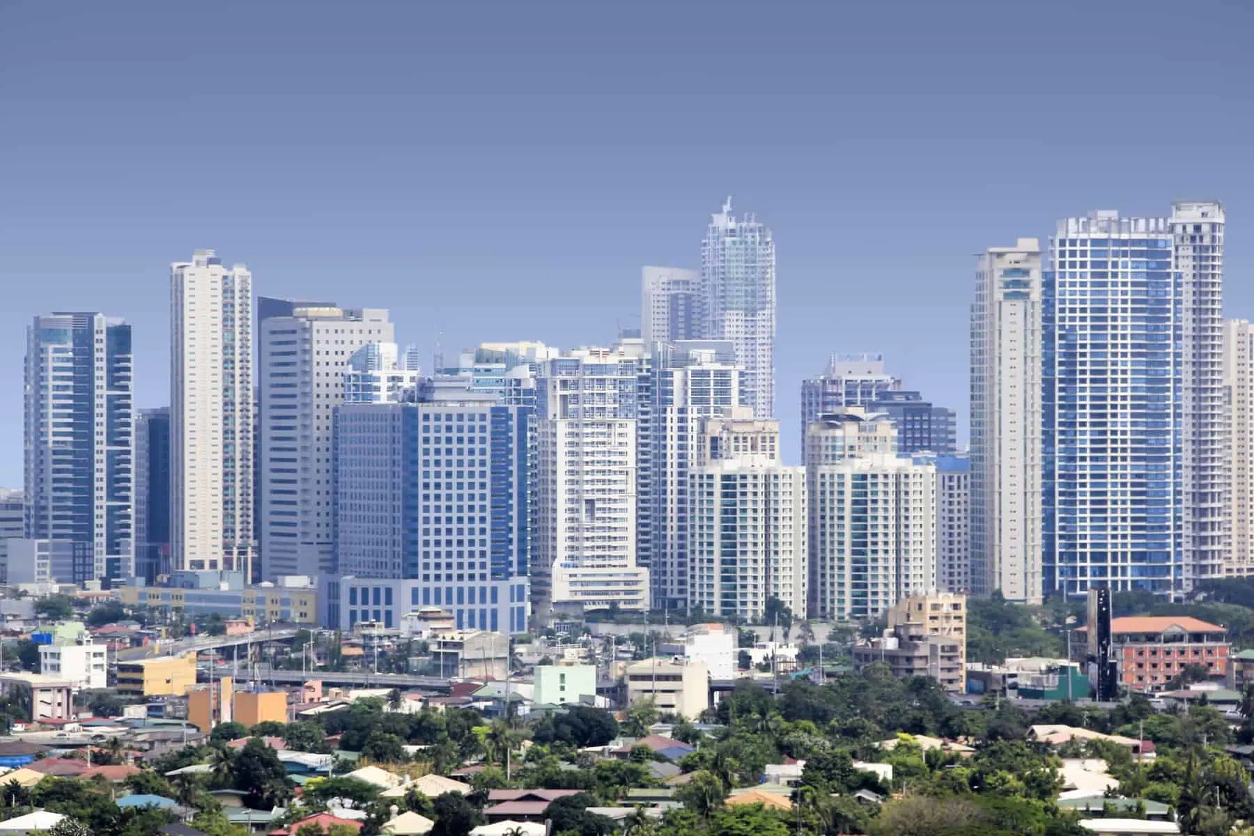 Colorful tuk-tuks and tall skyscrapers in a lively city street in Manila, Philippines.