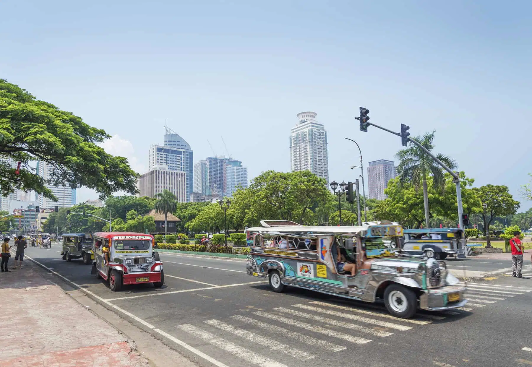 Colorful tuk-tuks and tall skyscrapers in a lively city street in Manila, Philippines.
