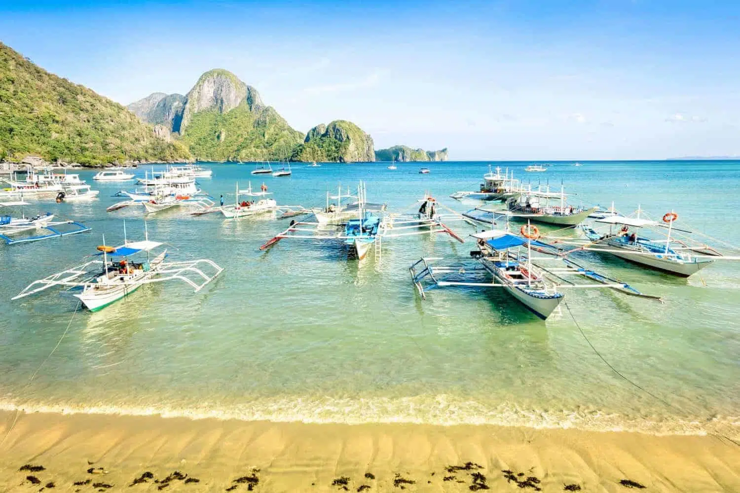 Vibrant tropical island cove with clear blue water and lush green mountains in the background.