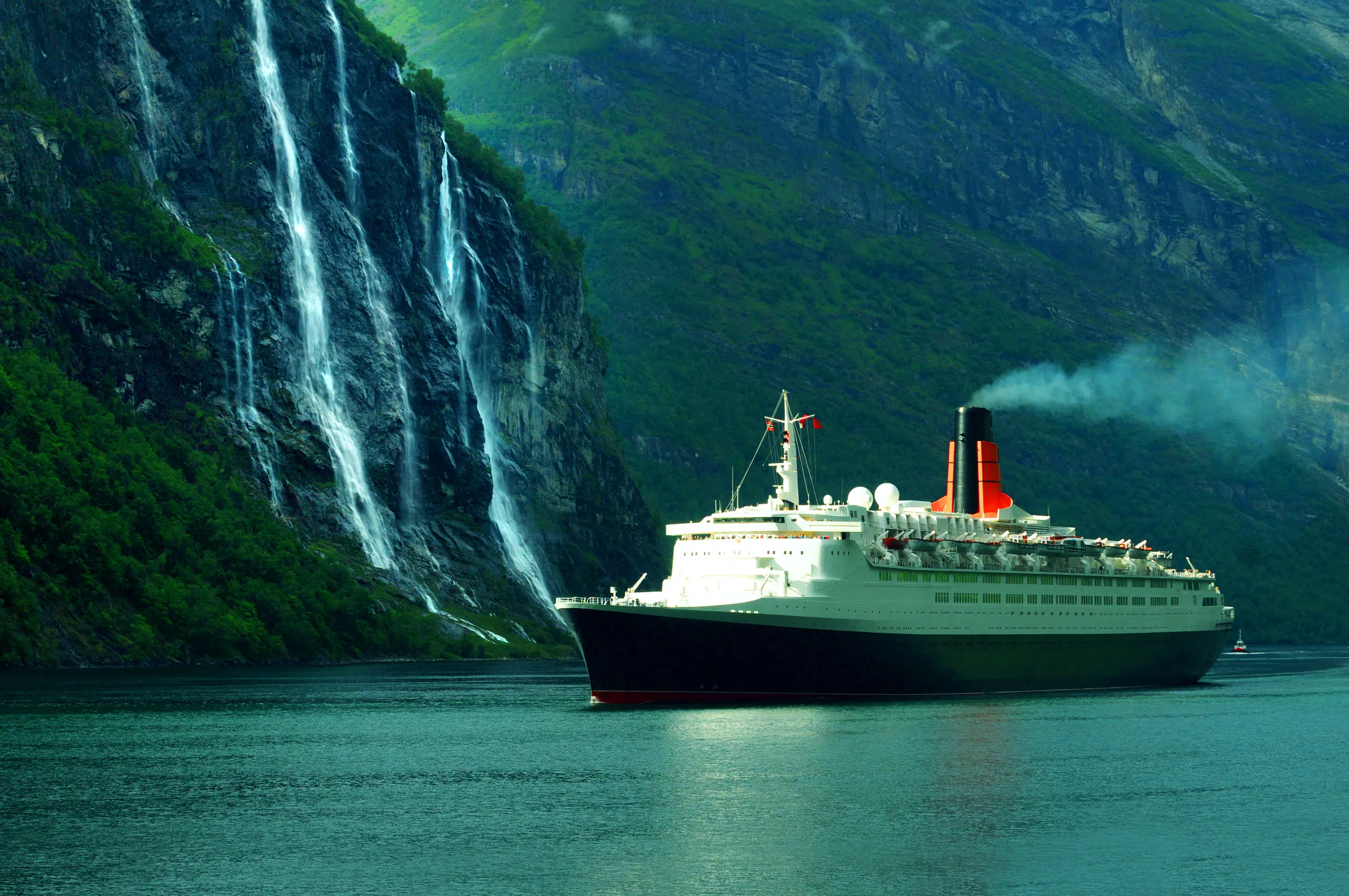 The famous Queen Elizabeth II cruise ship sailing in the ocean, along the Seven Sisters waterfall in Norway.