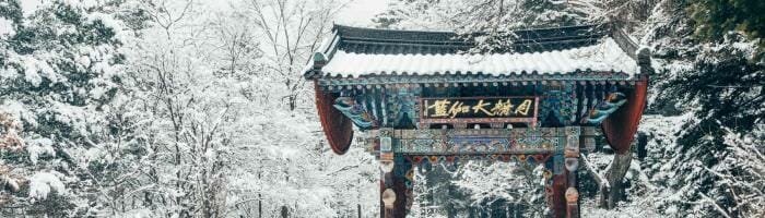 Snow-covered traditional Chinese gate in a winter park scene.