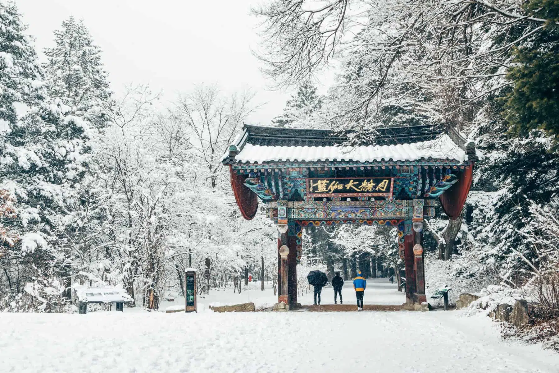 Snow-covered traditional Chinese gate in a winter park scene.