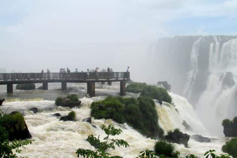 Waterfalls of the Iguazu River on the border of Argentina anf Brazili. Huge streams of water spray, numerous waterfalls, water mist. The clouds in the blue sky, tropical greenery around.