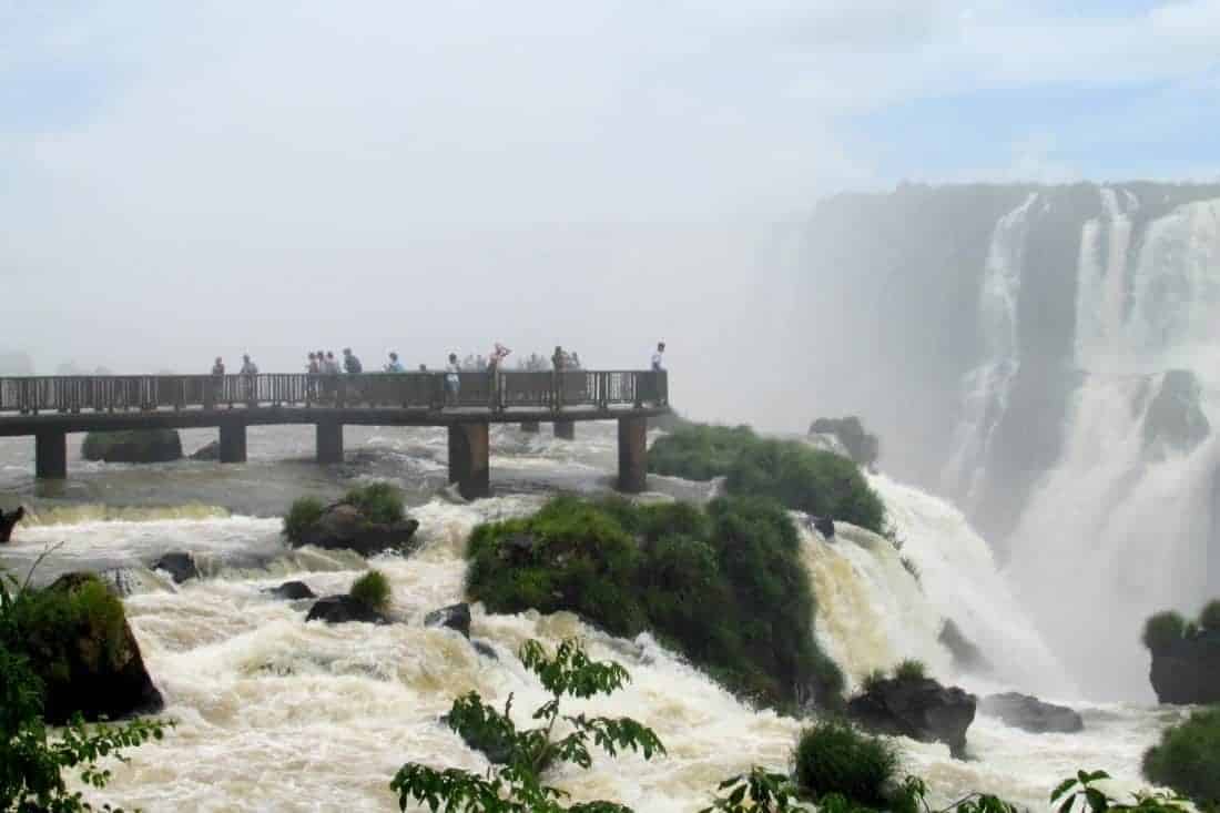 Waterfalls of the Iguazu River on the border of Argentina anf Brazili. Huge streams of water spray, numerous waterfalls, water mist. The clouds in the blue sky, tropical greenery around.
