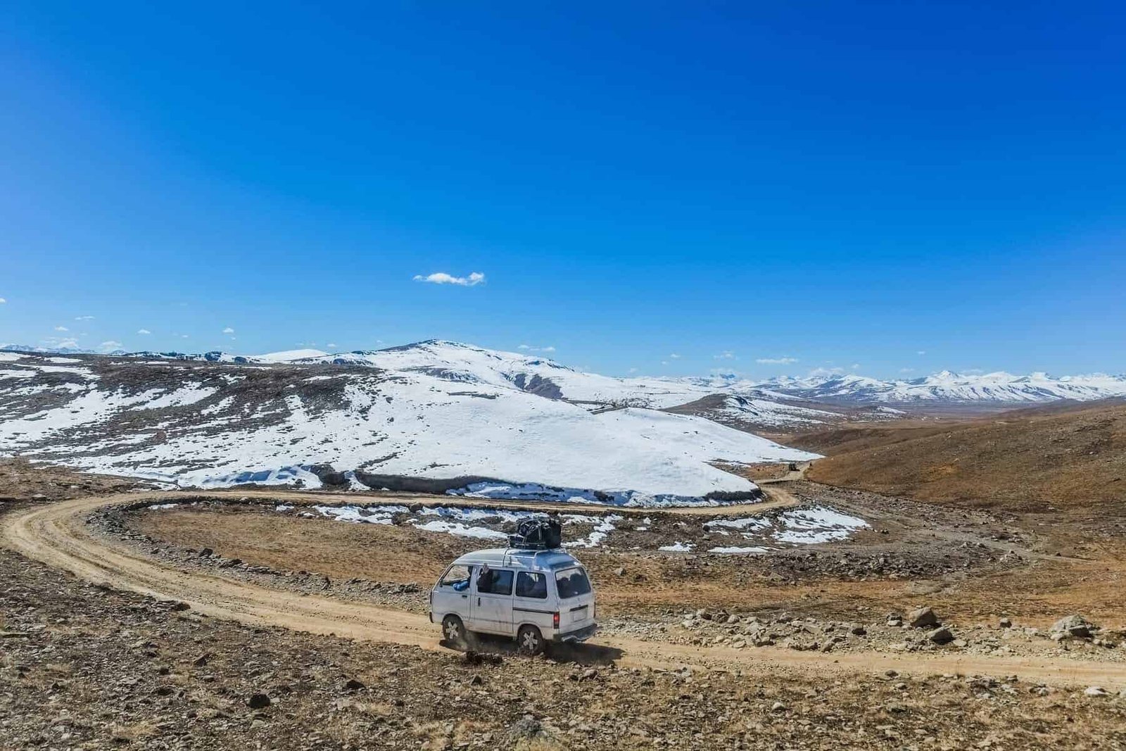 A white van with luggage on the roof running along the unpaved road. Deosai plains, Pakistan.