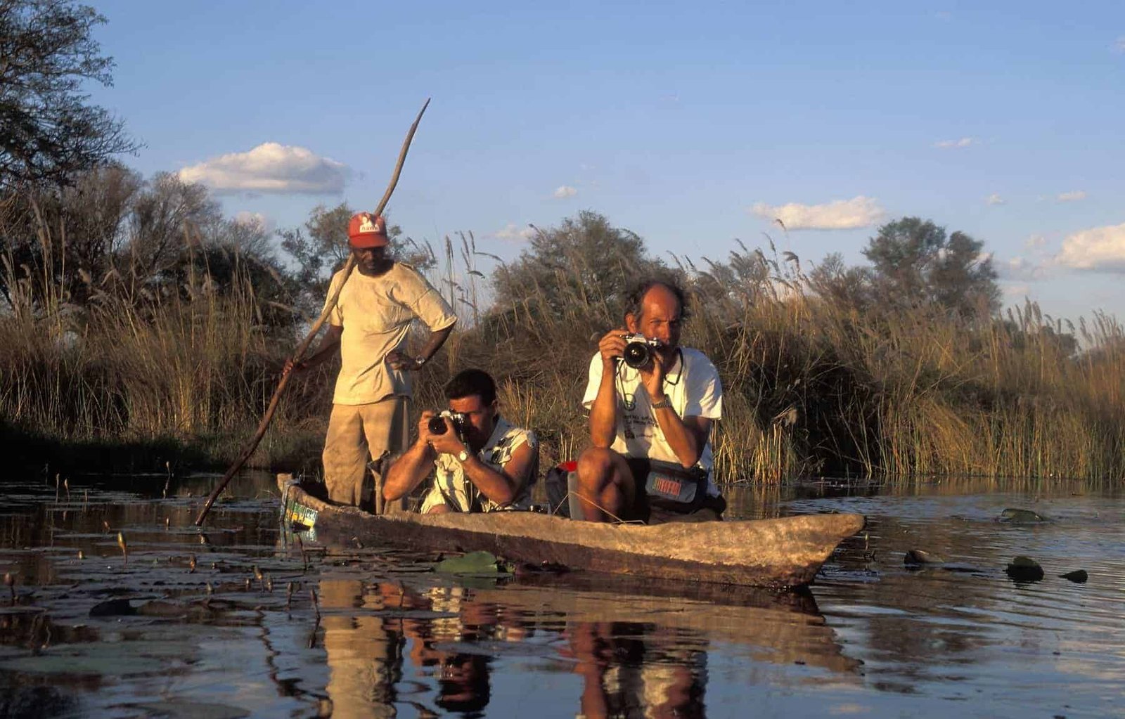 Tourists taking photos from a traditional canoe (mekoro). The mekoro is the typical boat used on the Okavango Delta in Botswana. Hewn from large trunked wild ebony, it is manoeuvred using one wooden pole.
