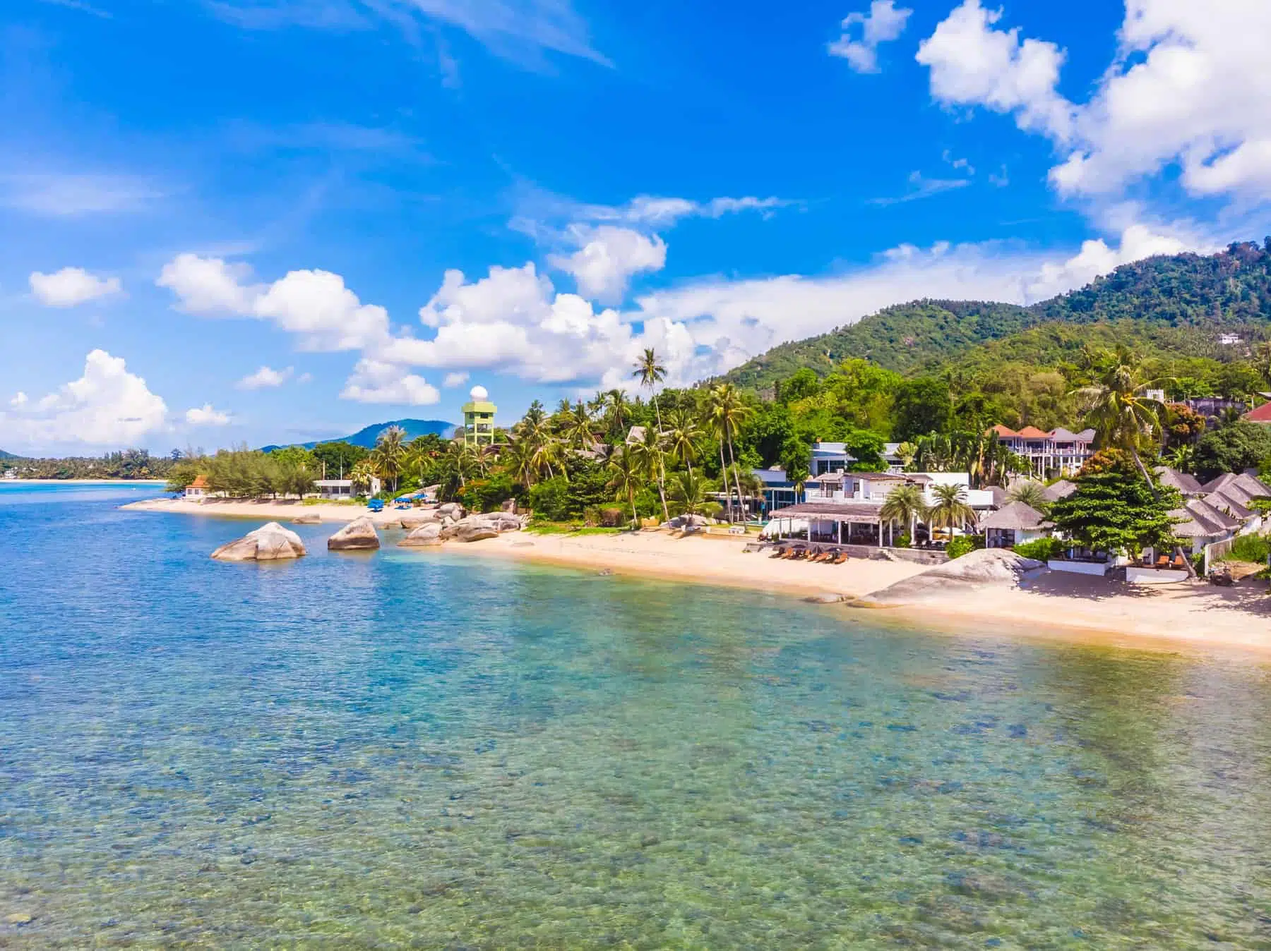 Lush green island with white sandy beach and turquoise waters, popular vacation destination in Thailand.