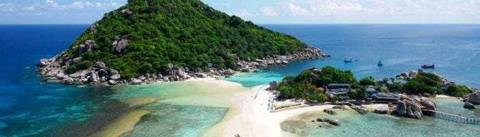 Lush green island with white sandy beach and turquoise waters, popular vacation destination in Thailand.