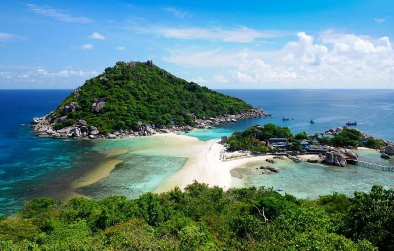Lush green island with white sandy beach and turquoise waters, popular vacation destination in Thailand.