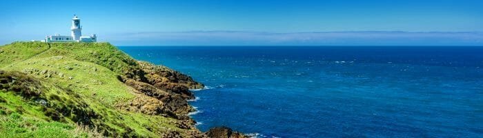Lighthouse on green cliff overlooking the ocean with blue sky, travel and coastal scenery.