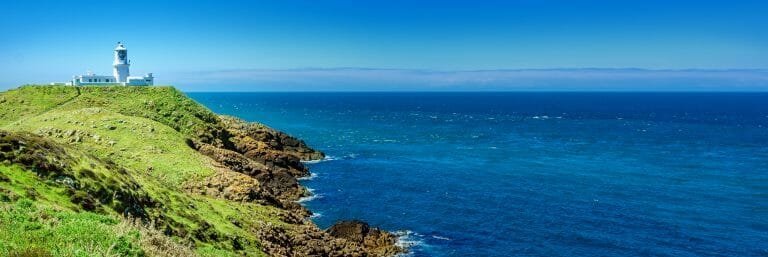 Lighthouse on green cliff overlooking the ocean with blue sky, travel and coastal scenery.