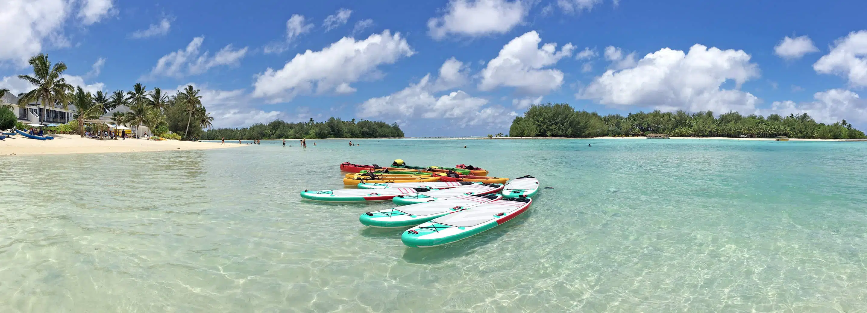 cook islands — Weathered boat on a beach with a rustic house and forested hills in the background.