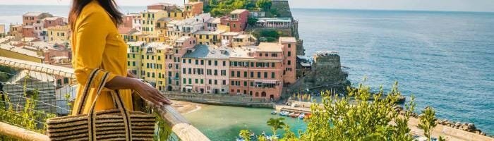 Colorful coastal village in Italy with a woman in a yellow dress and sun hat enjoying scenic ocean views.