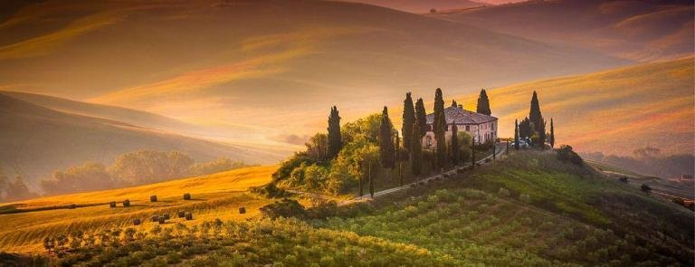 Rolling hills with a rustic mansion and cypress trees in Tuscany at sunset, perfect for vacation travel and relaxing getaways.