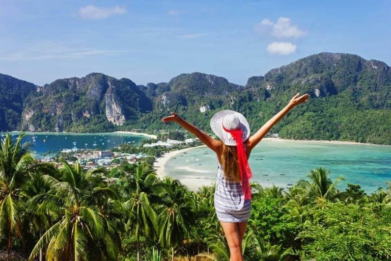 Breathtaking coastal view with turquoise waters, lush green mountains, and a woman enjoying a tropical vacation.