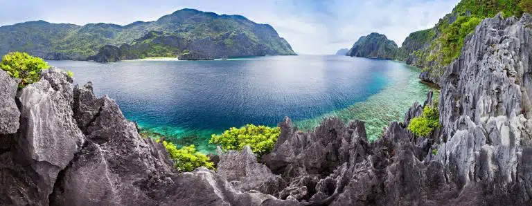 Vibrant tropical island cove with clear blue water and lush green mountains in the background.