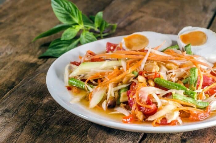 Freshly prepared chicken noodle soup with boiled eggs, fresh vegetables, and lime wedges on a rustic wooden table.