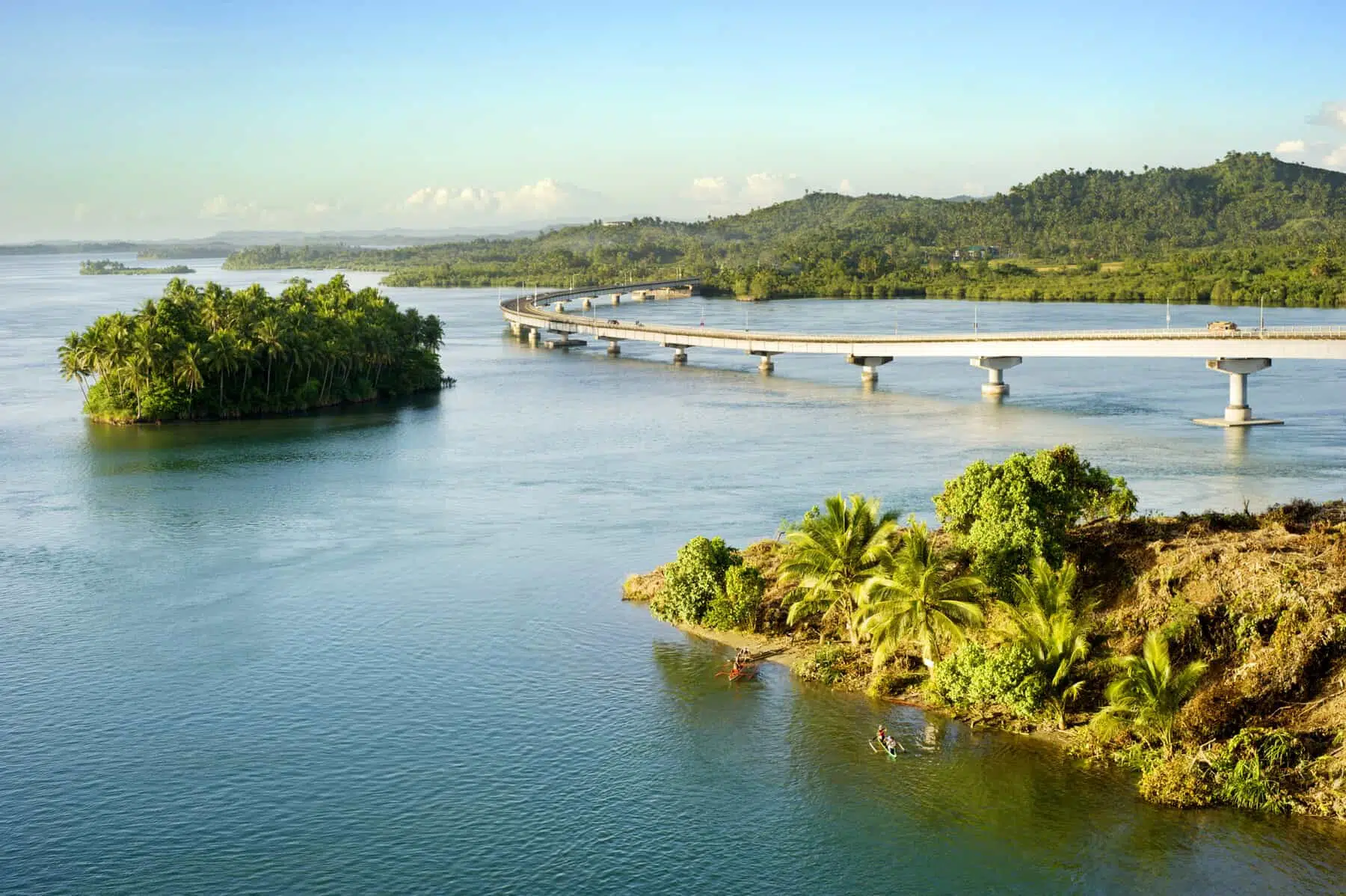 Vibrant tropical island cove with clear blue water and lush green mountains in the background.