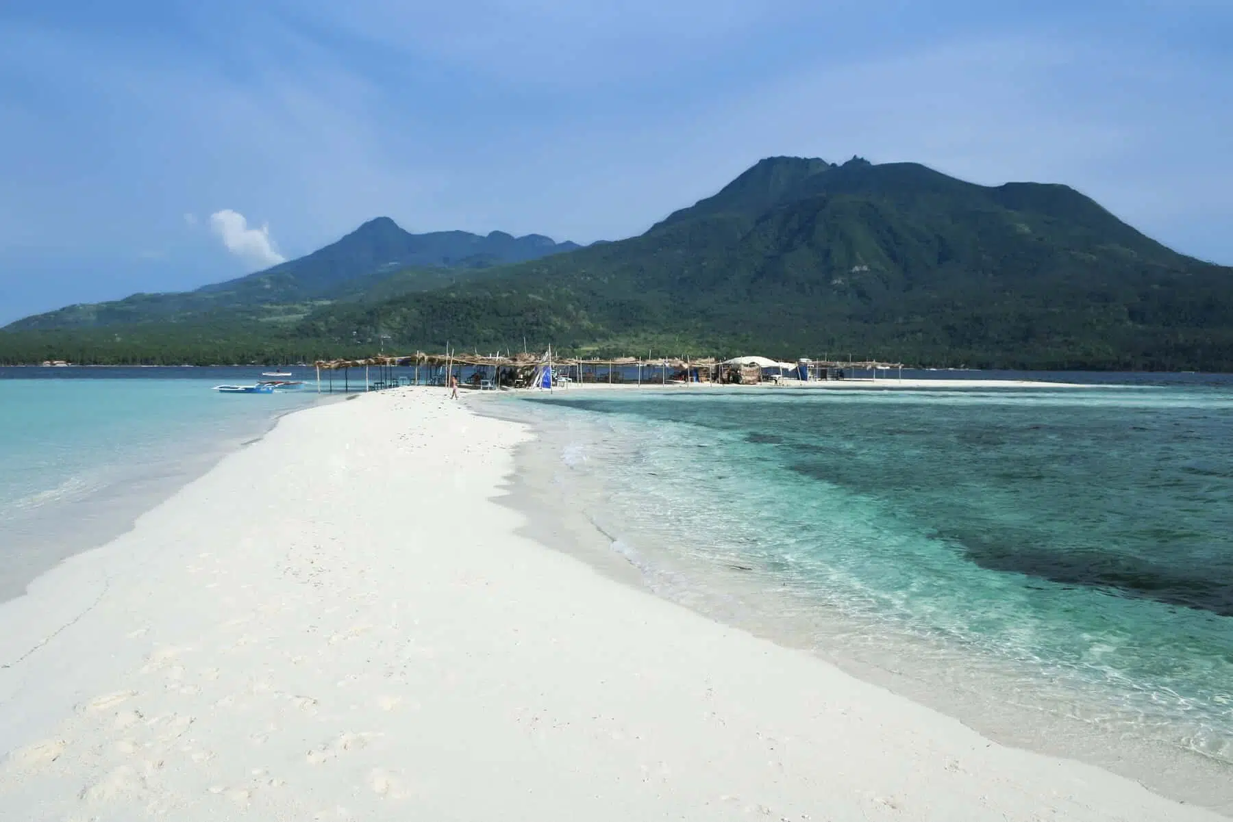 Vibrant tropical island cove with clear blue water and lush green mountains in the background.