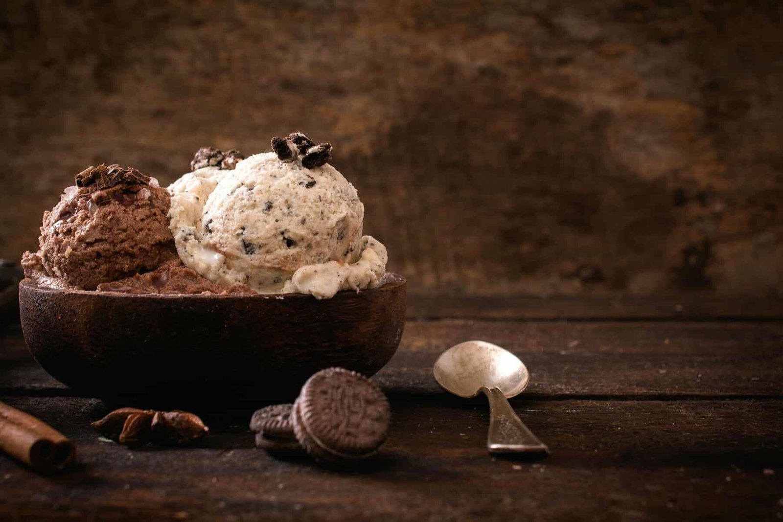 Creamy chocolate and cookies and cream ice cream scoops in a rustic wooden bowl.
