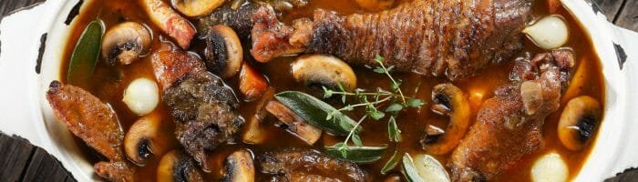 Rich beef stew with mushrooms, carrots, and herbs served in a rustic bowl on wooden table.