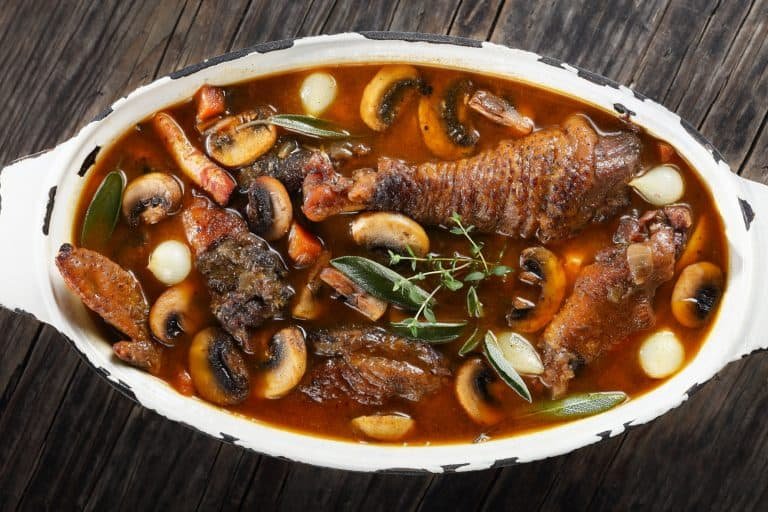 Rich beef stew with mushrooms, carrots, and herbs served in a rustic bowl on wooden table.