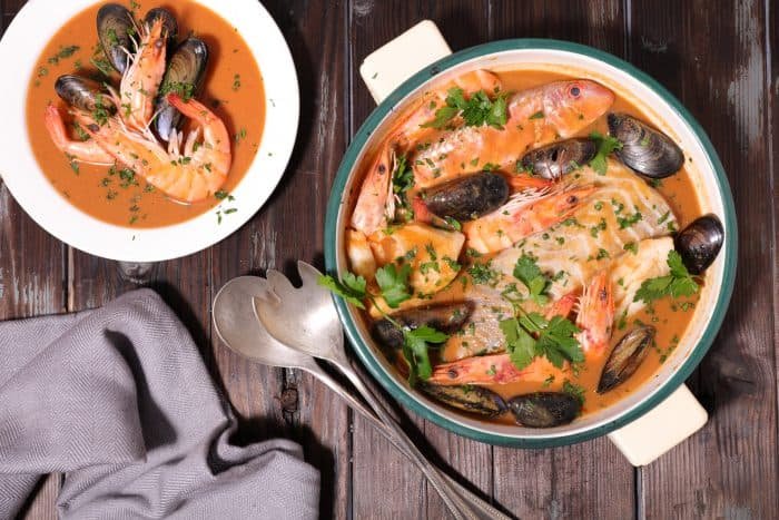 Bouillabaisse from Provence. Rich seafood and shellfish stew in a traditional ceramic dish, garnished with fresh herbs on rustic wooden table.