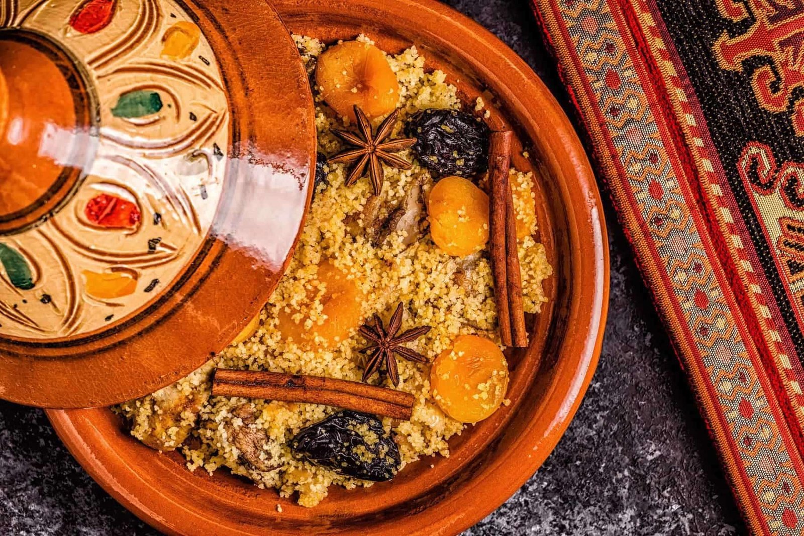 Scented couscous with dried fruits, cinnamon sticks, and star anise in traditional Moroccan pottery.