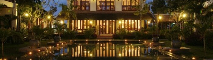 Luxurious tropical resort with illuminated main building at dusk, reflecting in the water.