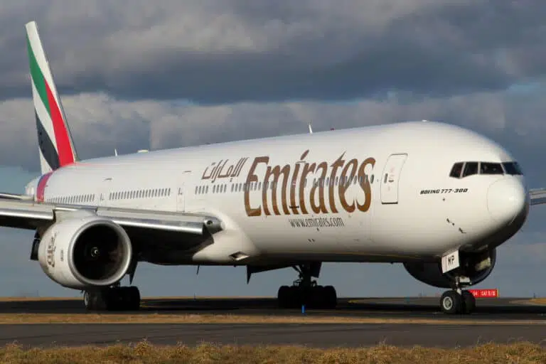 Boeing 777-300 Emirates airplane taxiing on runway under cloudy sky.