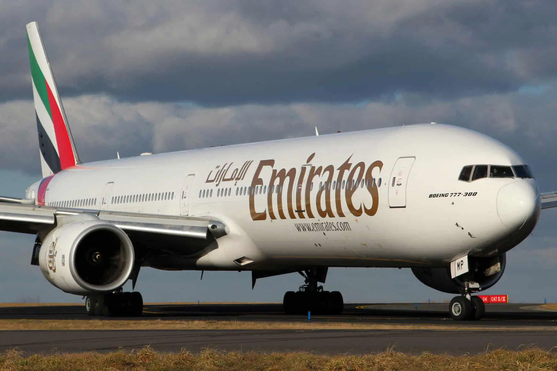 Boeing 777-300 Emirates airplane taxiing on runway under cloudy sky.