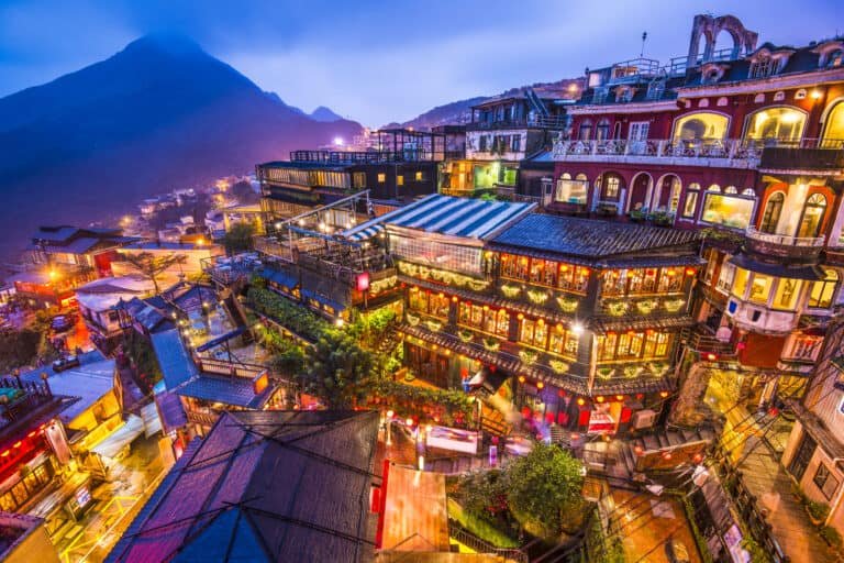 Colorful hillside resort with illuminated buildings at night, surrounded by mountains, perfect for vacation travel in Taiwan.