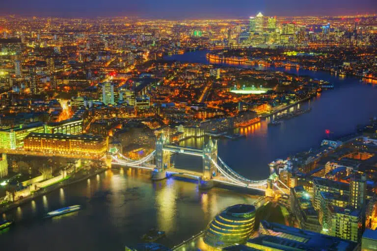 London skyline at night featuring Tower Bridge and Thames River, vibrant city lights, iconic landmarks, and modern skyscrapers.