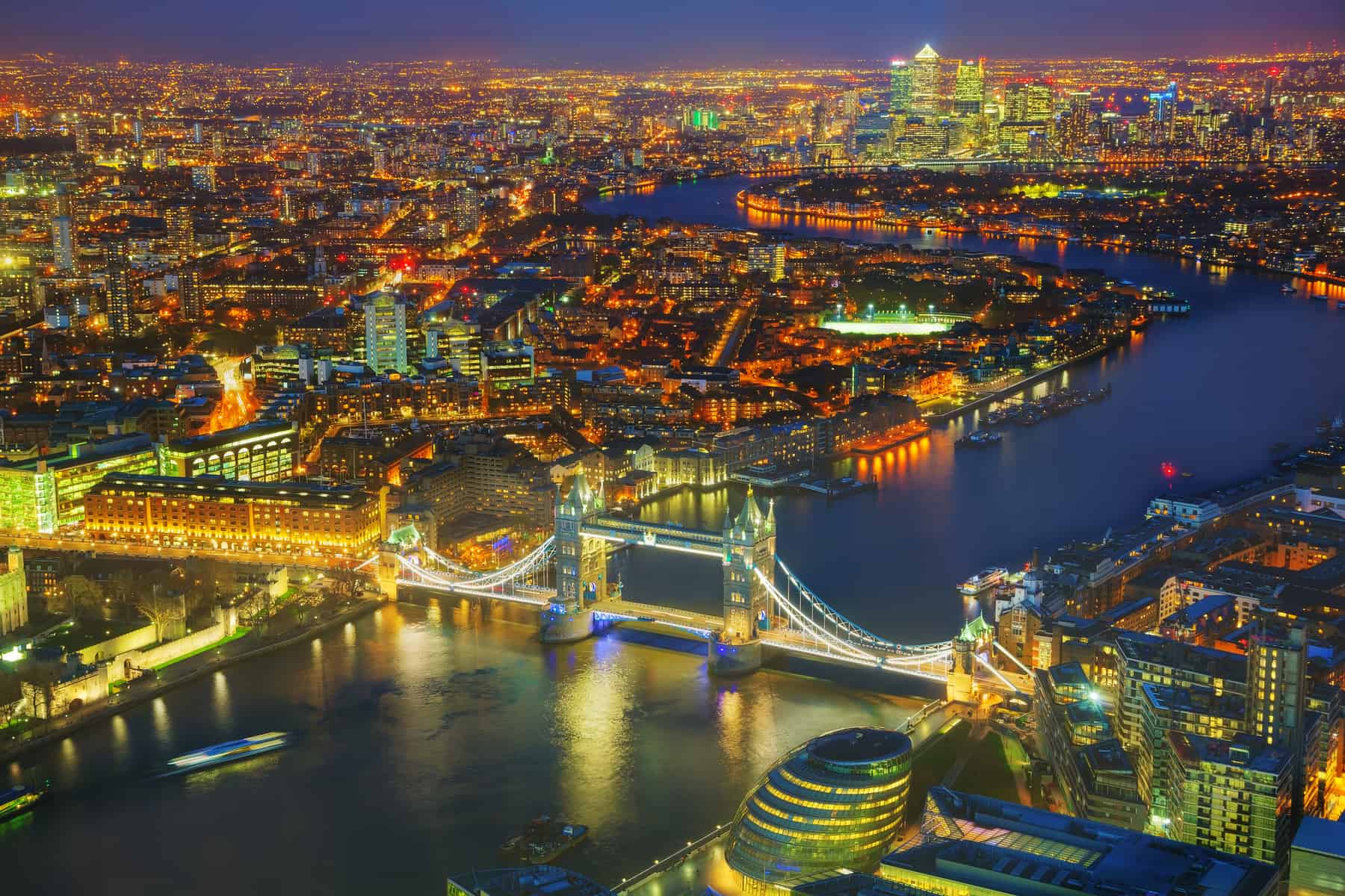 London skyline at night featuring Tower Bridge and Thames River, vibrant city lights, iconic landmarks, and modern skyscrapers.