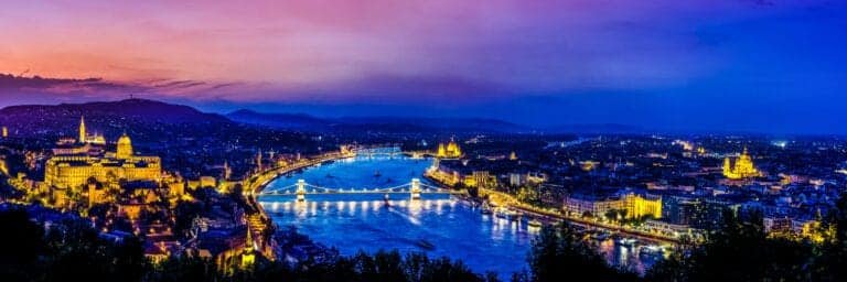 Budapest city skyline at dusk with illuminated Chain Bridge over Danube River and historic landmarks.
