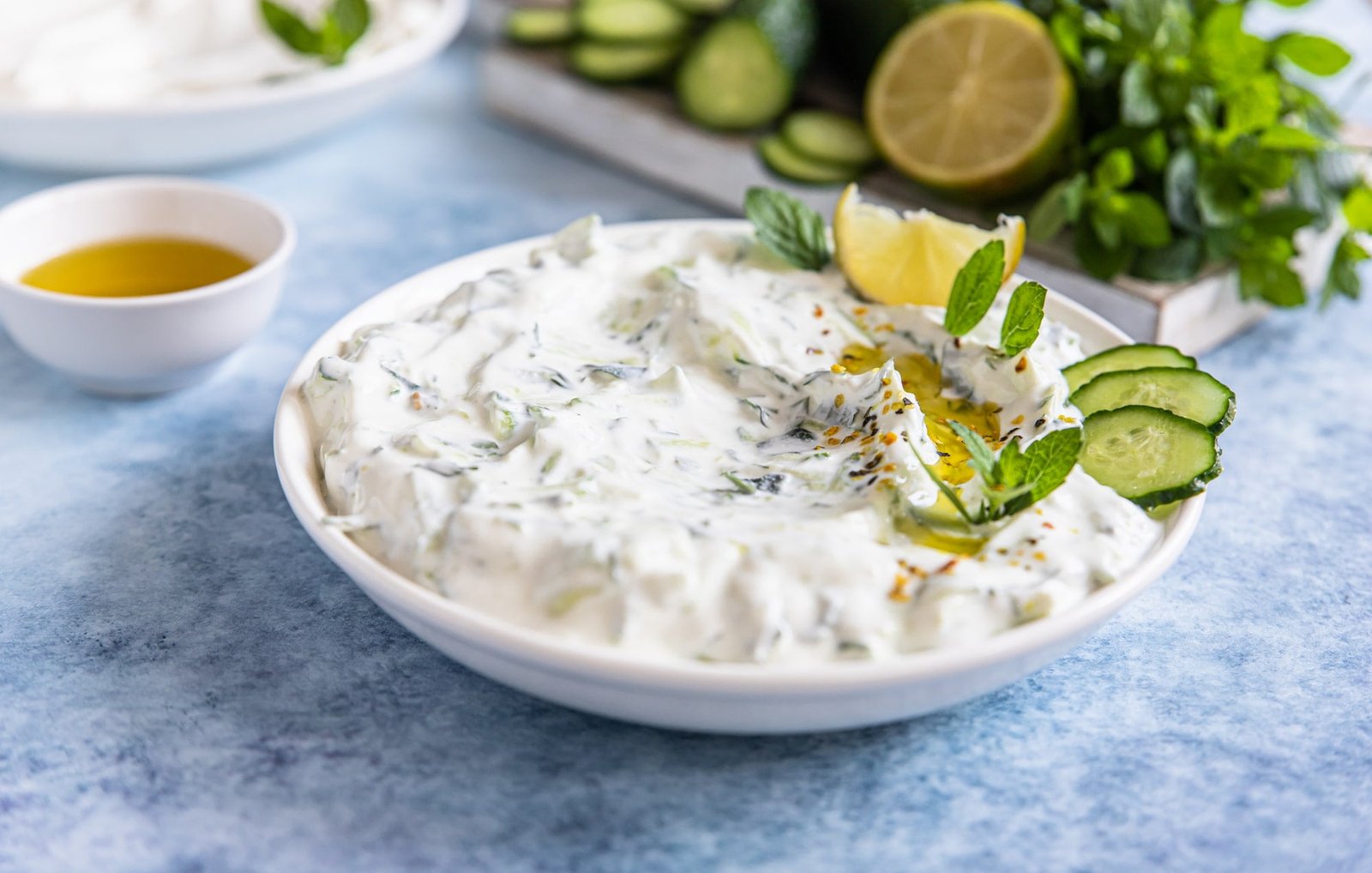 Indian Raita sauce or dip with cucumber, yoghurt, garlic and mint, blue concrete background. Traditional Indian cuisine.