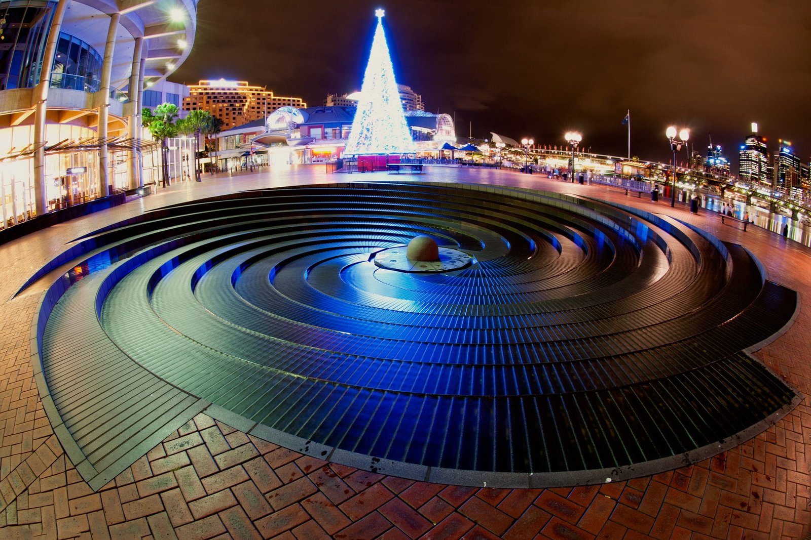 Christmas time in Darling Harbour, Sydney, Australia. Blue christmas tree in front of a rounded fountain.