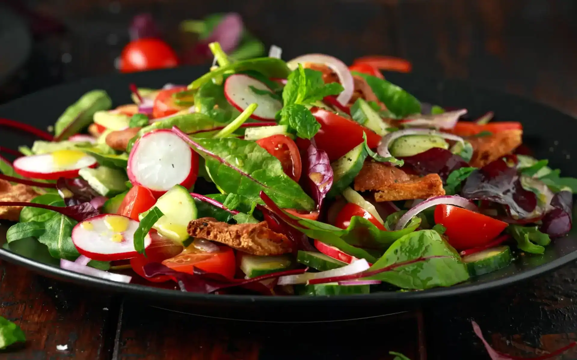 Traditional fattoush salad on a plate with pita croutons, cucumber, tomato, red onion, vegetables mix and herbs.