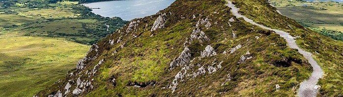 The hiking trail at the top of Diamond Hill in Connemara National Park, Ireland. Behind, the sun plays with the clouds reflected in the sea. Travel to Ireland. The greenest island in Europe.
