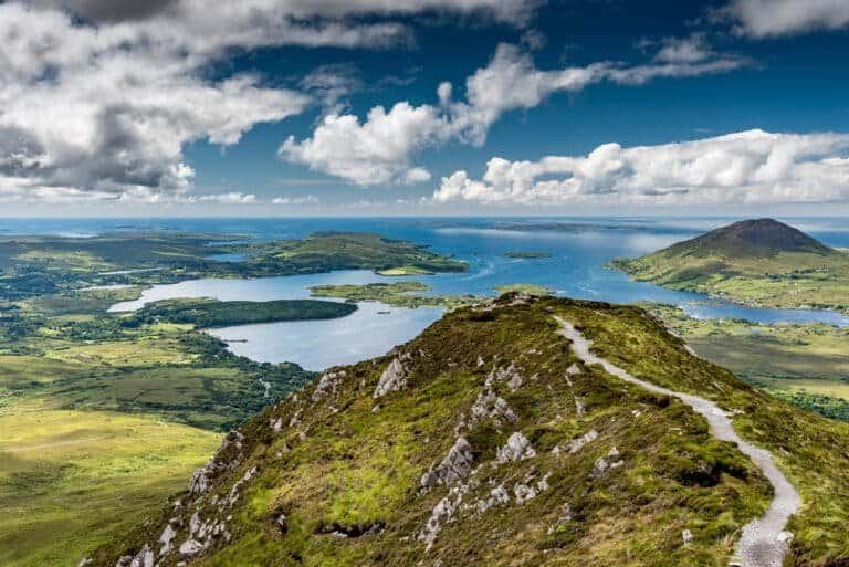 The hiking trail at the top of Diamond Hill in Connemara National Park, Ireland. Behind, the sun plays with the clouds reflected in the sea. Travel to Ireland. The greenest island in Europe.