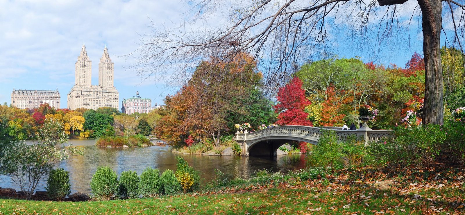 New York City Central Park panorama view in Autumn with Manhattan skyscrapers and colorful trees with Rainbow Bridge over lake with reflection.