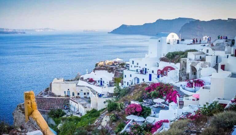 Picturesque village Santorini Greece on volcanic island with whitewashed buildings and vibrant pink bougainvillea flowering plants overlooking the Aegean Sea.