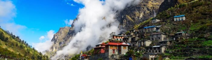 Charming mountain village with traditional houses in a lush green valley under blue sky and clouds near Himalayan peaks.