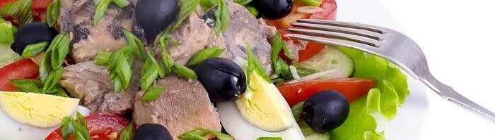 Fresh Mediterranean tuna salad with vegetables, eggs, and olives on white plate.